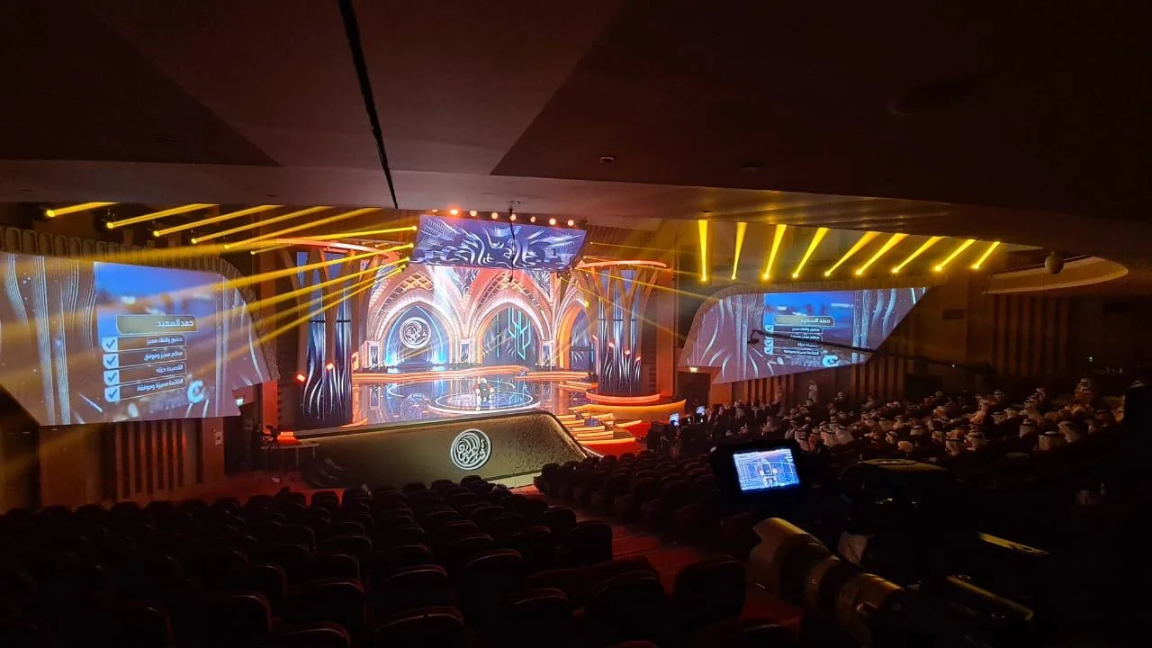 Theatrical live stage with warm lighting and a seated audience